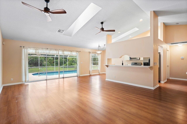 unfurnished living room with plenty of natural light, ceiling fan, wood-type flooring, and a skylight