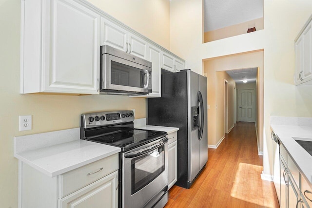 kitchen with white cabinets, appliances with stainless steel finishes, light wood-type flooring, and a high ceiling