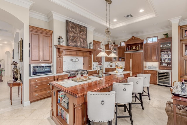 kitchen with wine cooler, sink, a center island with sink, appliances with stainless steel finishes, and pendant lighting