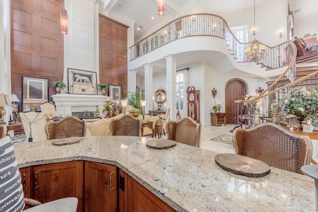 kitchen featuring ornate columns, a towering ceiling, a fireplace, decorative light fixtures, and light stone countertops