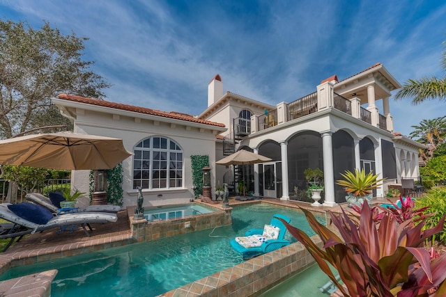 back of property featuring a sunroom, a balcony, and an in ground hot tub