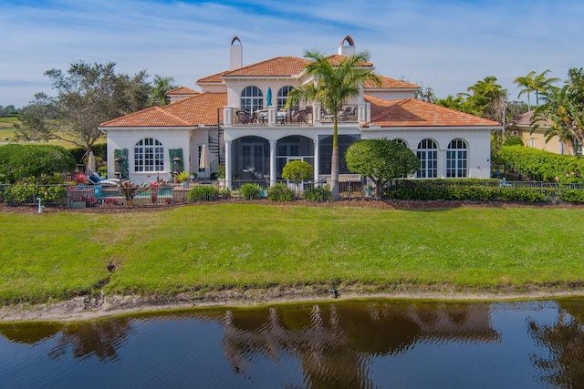 rear view of house featuring a water view, a balcony, and a lawn