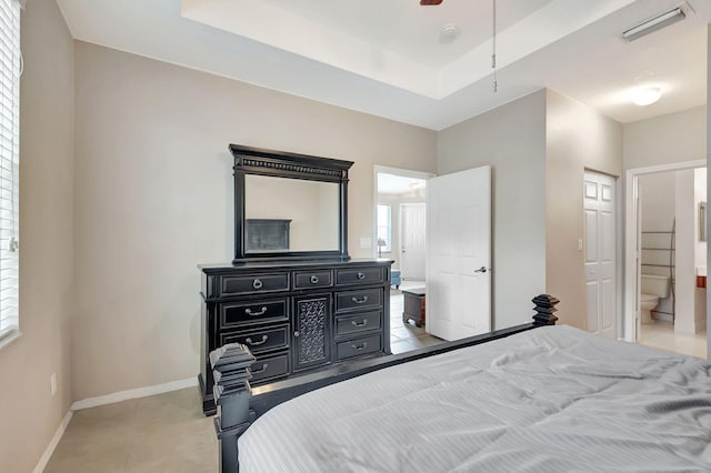 bedroom featuring a raised ceiling, ensuite bathroom, and light tile floors