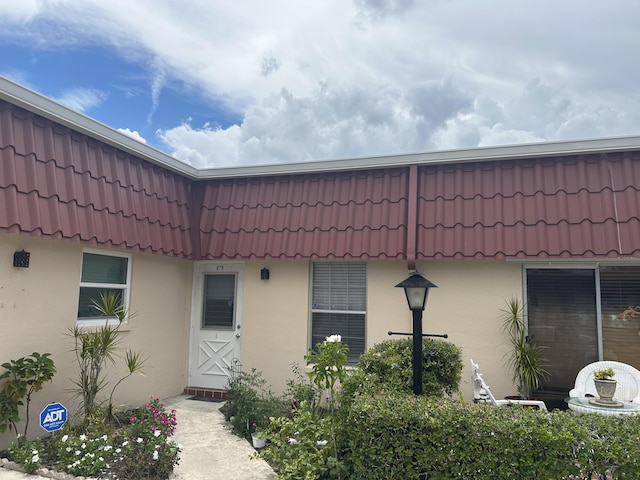 doorway to property featuring a tile roof, mansard roof, and stucco siding