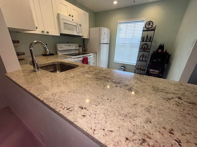 kitchen with white cabinetry, sink, light stone countertops, and white appliances