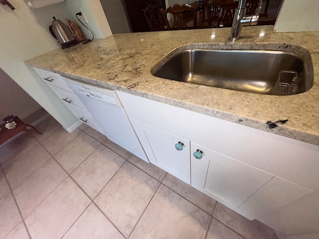 room details featuring light stone countertops, sink, white cabinetry, and light tile floors