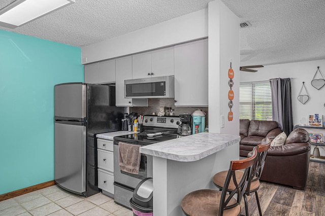 kitchen featuring ceiling fan, light hardwood / wood-style flooring, kitchen peninsula, stainless steel appliances, and a breakfast bar