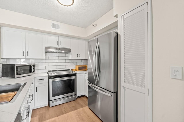 127 Yacht Club Way Unit 206, Hypoluxo, FL 33462 - kitchen featuring stainless steel appliances, visible vents, under cabinet range hood, light wood finished floors, and white cabinetry