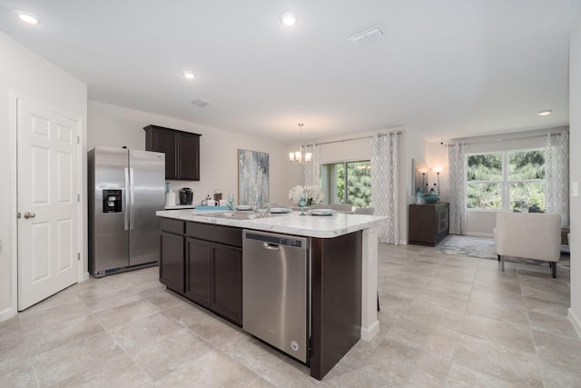 kitchen with plenty of natural light, an island with sink, stainless steel appliances, and a notable chandelier