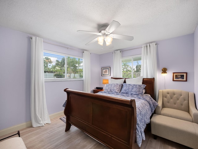 bedroom featuring multiple windows, a textured ceiling, light hardwood / wood-style floors, and ceiling fan