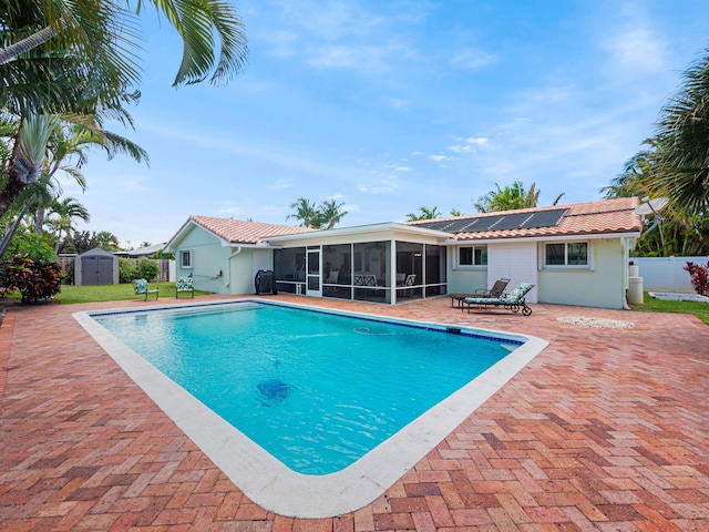 view of pool featuring a patio area, a sunroom, and a storage shed