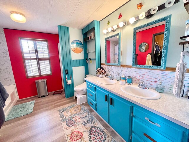 bathroom with a textured ceiling, wood-type flooring, tasteful backsplash, vanity, and toilet