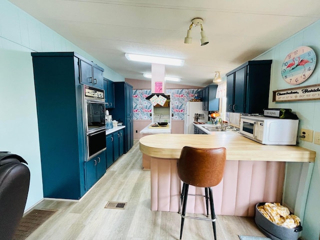 kitchen with blue cabinetry, sink, light hardwood / wood-style flooring, and kitchen peninsula