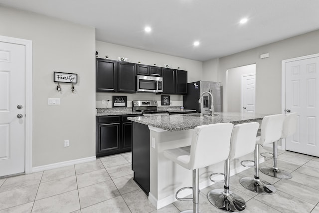 kitchen featuring light stone counters, stainless steel appliances, sink, a breakfast bar area, and an island with sink