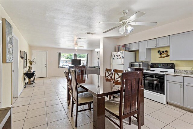 kitchen featuring light tile patterned floors, white appliances, gray cabinets, and light stone counters