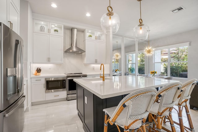 kitchen with white cabinets, decorative light fixtures, wall chimney range hood, stainless steel appliances, and sink