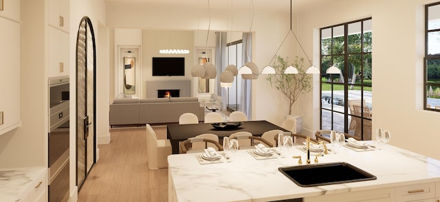 kitchen with pendant lighting, light stone counters, white cabinets, and sink