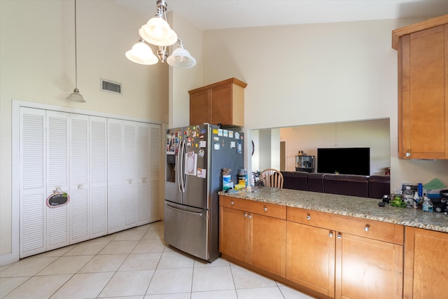 kitchen with high vaulted ceiling, hanging light fixtures, stainless steel fridge, and light stone counters