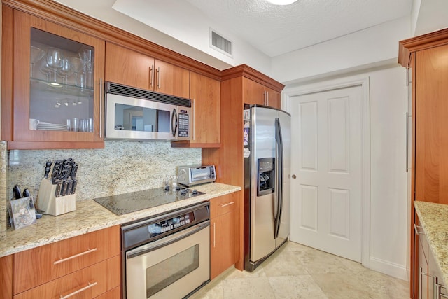 kitchen with tasteful backsplash, light tile flooring, a textured ceiling, light stone counters, and appliances with stainless steel finishes