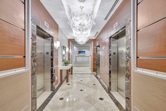 corridor with a chandelier, light tile flooring, a tray ceiling, and elevator