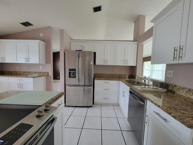 kitchen featuring lofted ceiling, white cabinets, light tile patterned floors, a textured ceiling, and appliances with stainless steel finishes