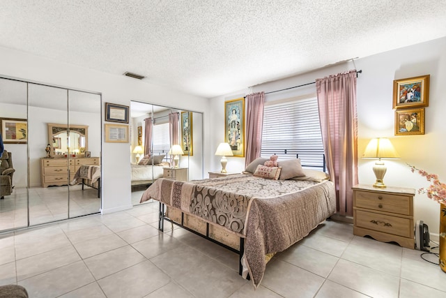 bedroom featuring multiple closets, light tile patterned flooring, a textured ceiling, and visible vents