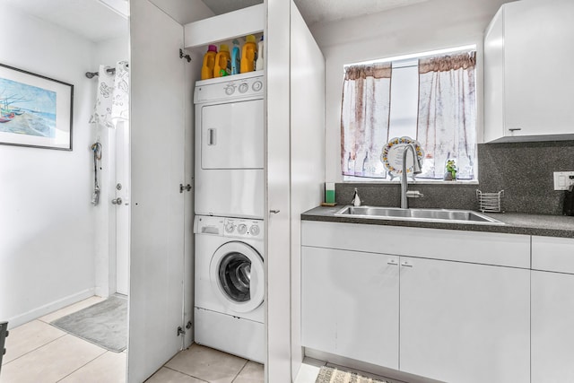 laundry area featuring laundry area, a sink, light tile patterned floors, and stacked washer / drying machine