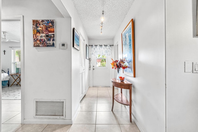 hallway featuring light tile patterned floors, baseboards, a textured ceiling, and visible vents