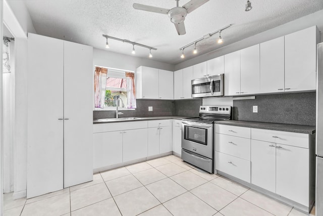 kitchen with ceiling fan, backsplash, appliances with stainless steel finishes, dark countertops, and a sink