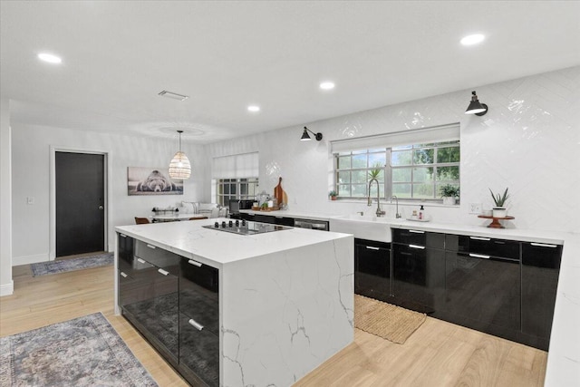 kitchen with decorative light fixtures, black electric stovetop, a kitchen island, sink, and light hardwood / wood-style flooring