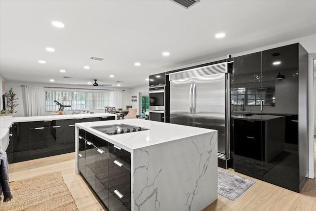 kitchen with light stone countertops, a kitchen island, stainless steel appliances, light wood-type flooring, and ceiling fan