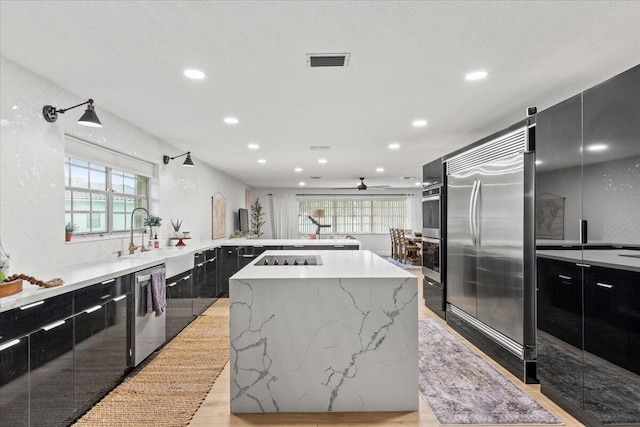 kitchen featuring ceiling fan, a kitchen island, a wealth of natural light, sink, and appliances with stainless steel finishes