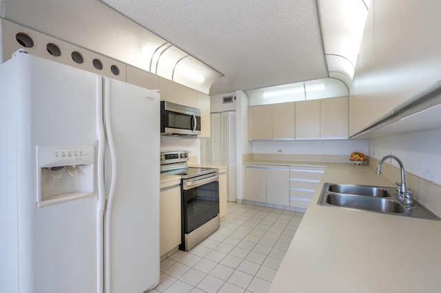 kitchen featuring light tile patterned floors, light countertops, appliances with stainless steel finishes, a sink, and a textured ceiling