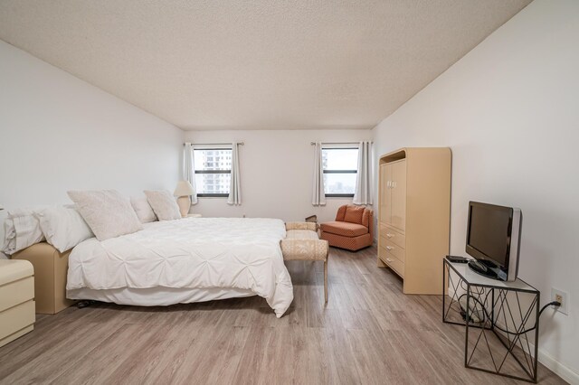 bedroom with lofted ceiling, a textured ceiling, and light wood finished floors