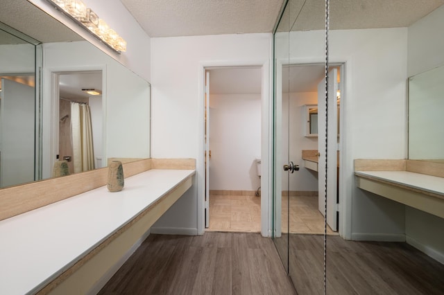 full bathroom with a textured ceiling, wood finished floors, vanity, and baseboards