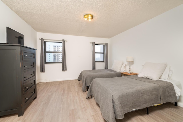 bedroom featuring light wood-style flooring, baseboards, and a textured ceiling