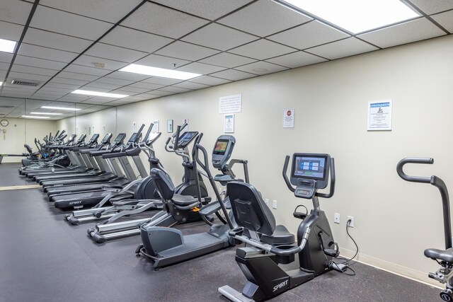 exercise room with a paneled ceiling, visible vents, and baseboards