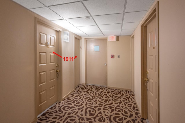 corridor with a paneled ceiling and baseboards