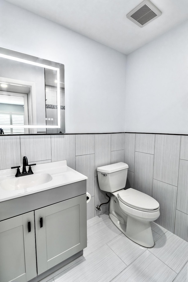 bathroom with tile patterned floors, vanity, tile walls, and toilet