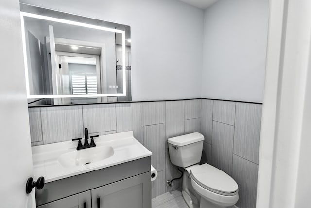 bathroom with vanity, toilet, and tile walls