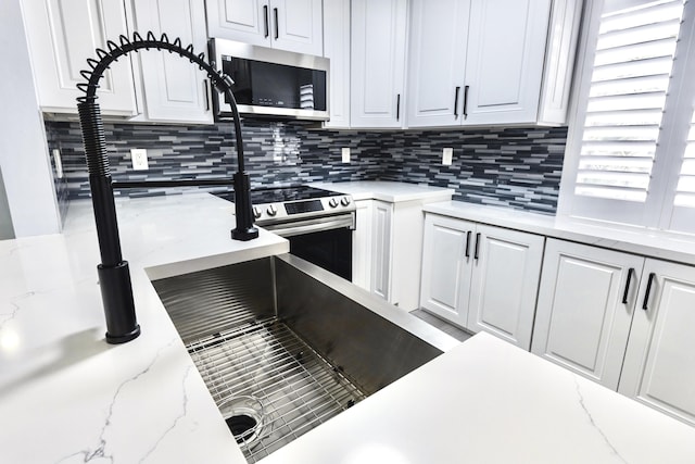 kitchen with tasteful backsplash, light stone countertops, white cabinets, and stainless steel appliances