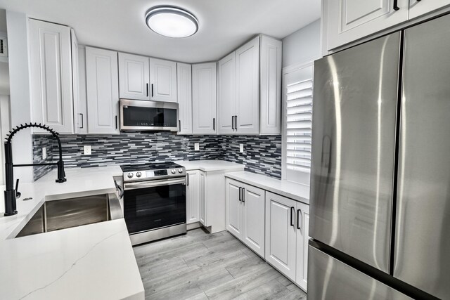 kitchen with sink, white cabinets, light wood-type flooring, and appliances with stainless steel finishes