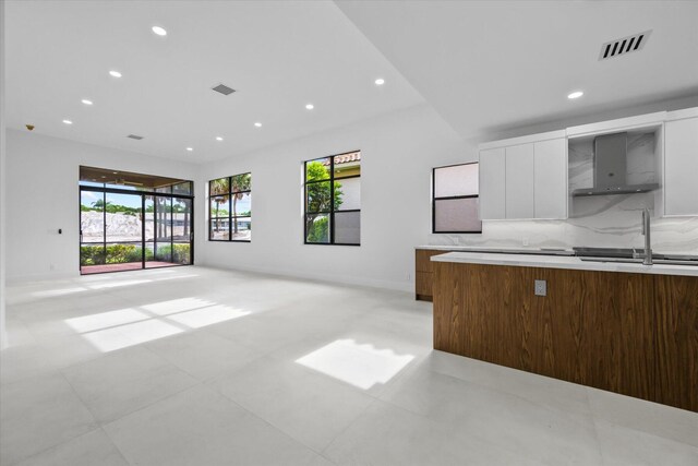 kitchen with decorative backsplash, white cabinetry, sink, and wall chimney range hood