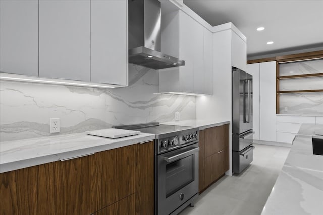 kitchen featuring tasteful backsplash, white cabinets, high end appliances, light stone counters, and wall chimney exhaust hood