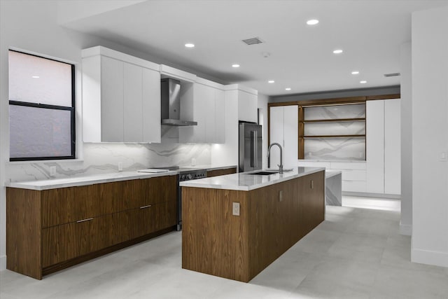 kitchen with white cabinetry, an island with sink, and wall chimney range hood