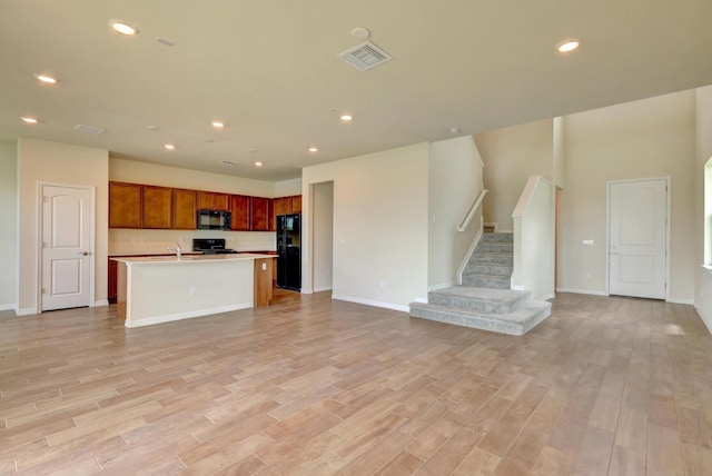 kitchen with an island with sink, black appliances, and light wood-type flooring