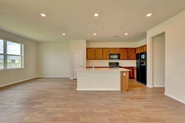 kitchen with a center island with sink, light hardwood / wood-style flooring, black appliances, and sink