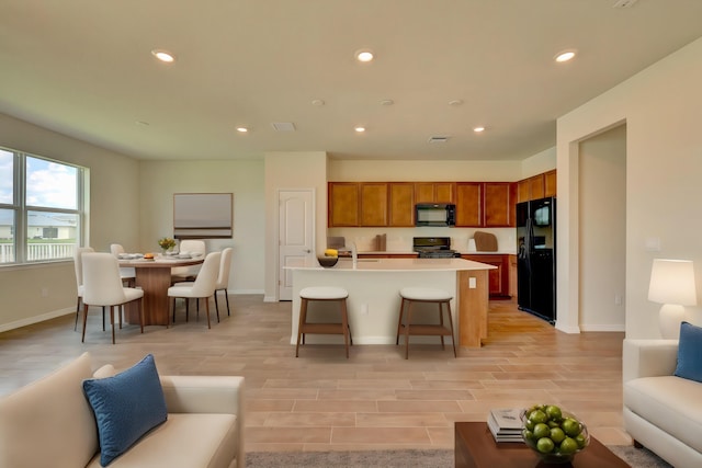 kitchen with a kitchen breakfast bar, sink, a center island with sink, and black appliances