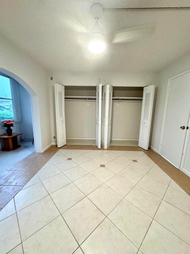 unfurnished bedroom featuring light tile patterned flooring, ceiling fan, and two closets