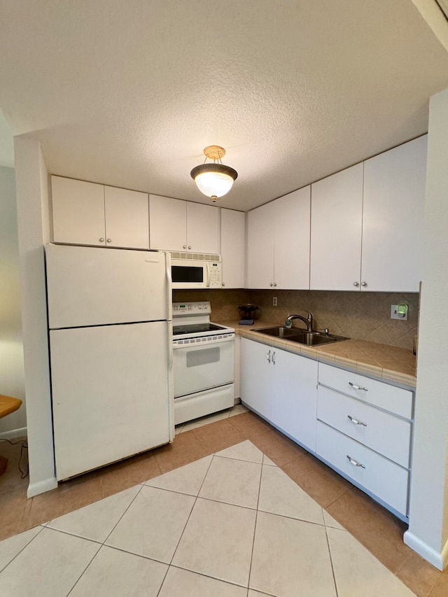 kitchen with tasteful backsplash, white appliances, white cabinets, sink, and light tile patterned flooring